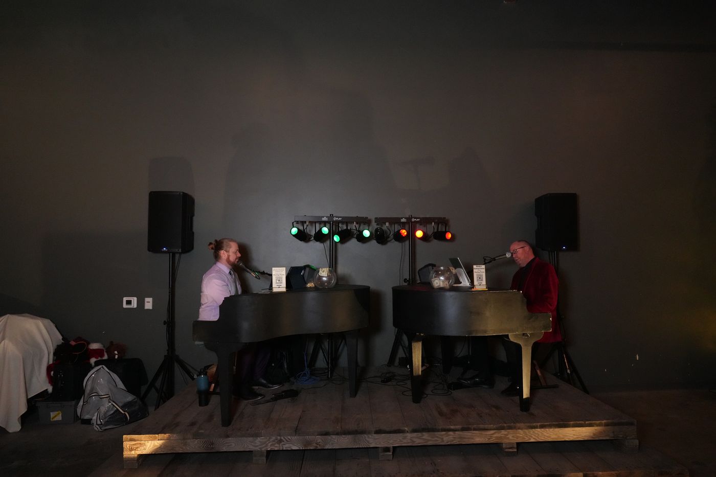 Indoor stage with twin pianos, PA speakers, and colored stage lights